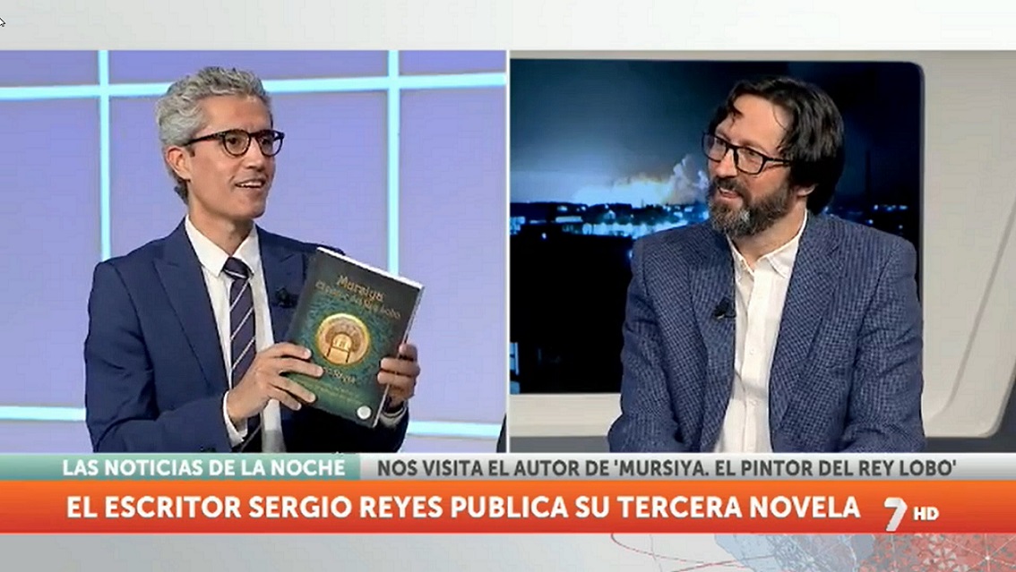 Luis Alcázar con un ejemplar de "Mursiya. El pintor del Rey Lobo" habla con su autor en las noticias de la noche de la 7 TV Región de Murcia