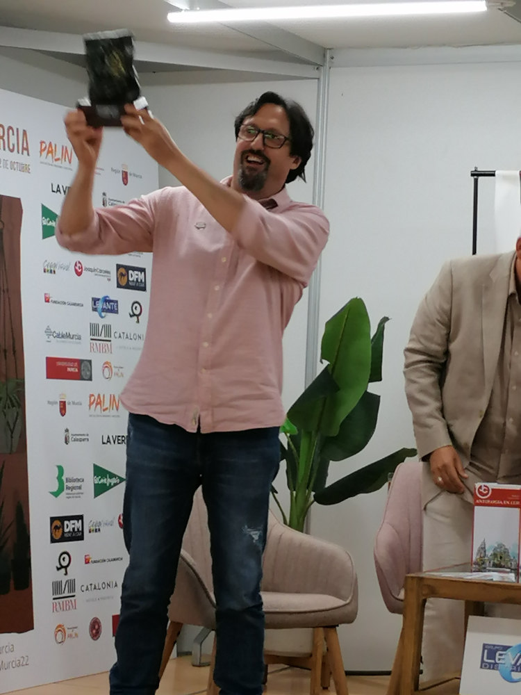 Sergio Reyes esgrime el busto que le ha sido entregado en el acto de entrega de premios del concurso de relato corto JC por la Cultura promovido por Inmobiliaria Joaquín Cárceles en la Feria del libro 2022