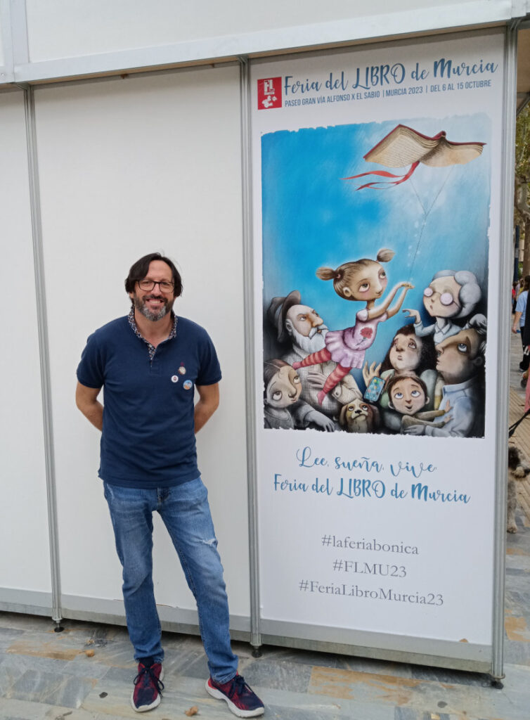 Sergio Reyes posa junto a la cartelería de la XXX Feria del libro de Murcia 2023